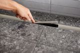 Tuyau de drainage Geberit CleanLine30 en acier inoxydable brossé, de 30 à 110 cm de long, sur carrelage gris.