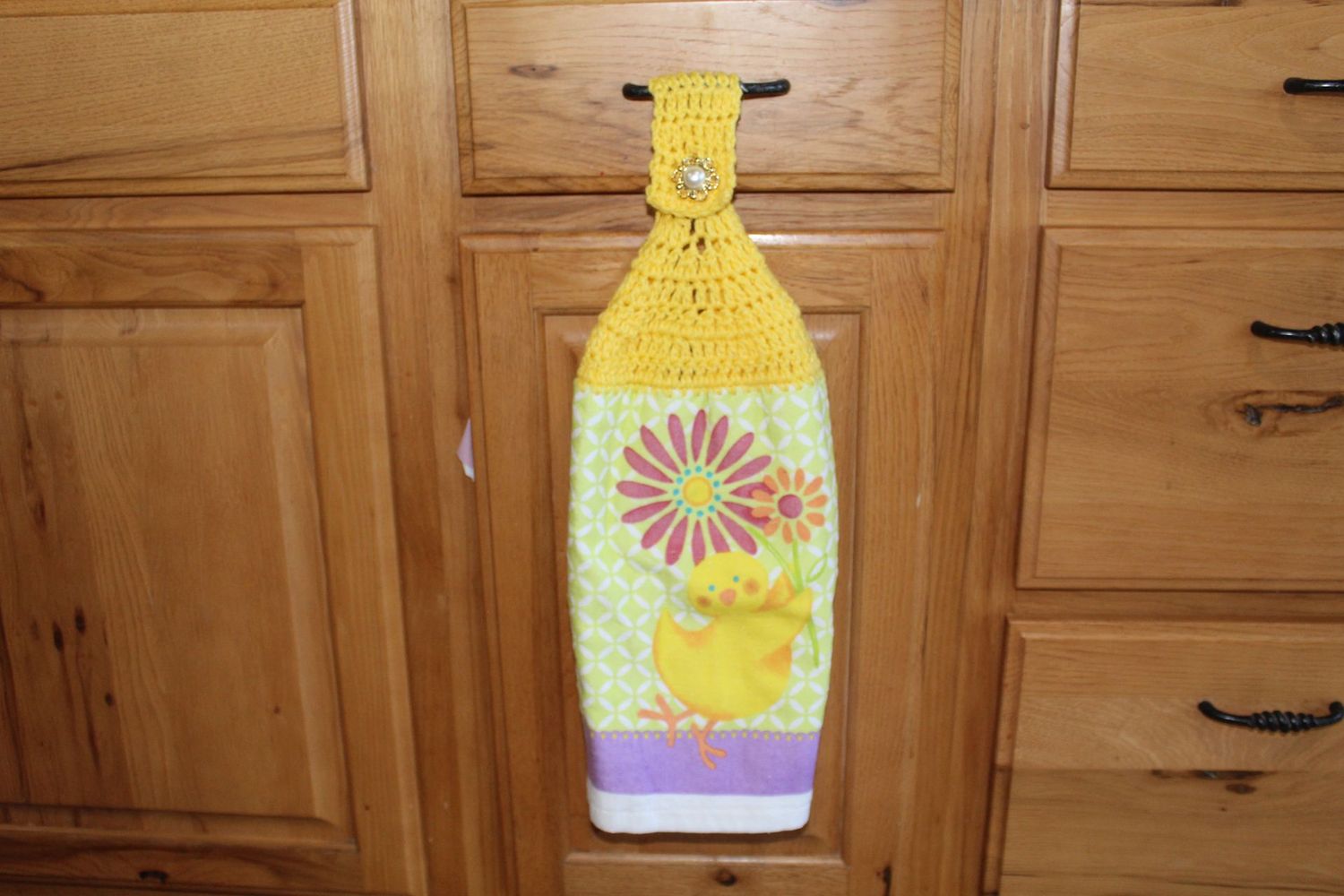 Easter chick kitchen towel with yellow crochet top and spring flower pattern hanging on cabinet handle.