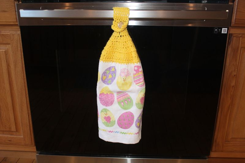 Easter hanging dish towel with bright yellow crocheted topper and pastel egg and chick pattern for spring kitchen decor.