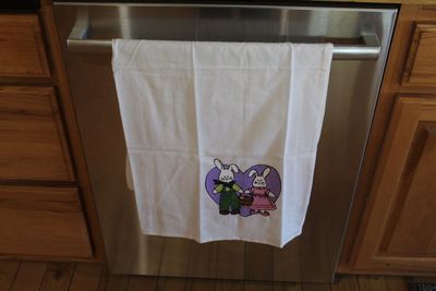 Hand painted Easter bunny couple kitchen towel with rabbits holding basket and purple heart background.