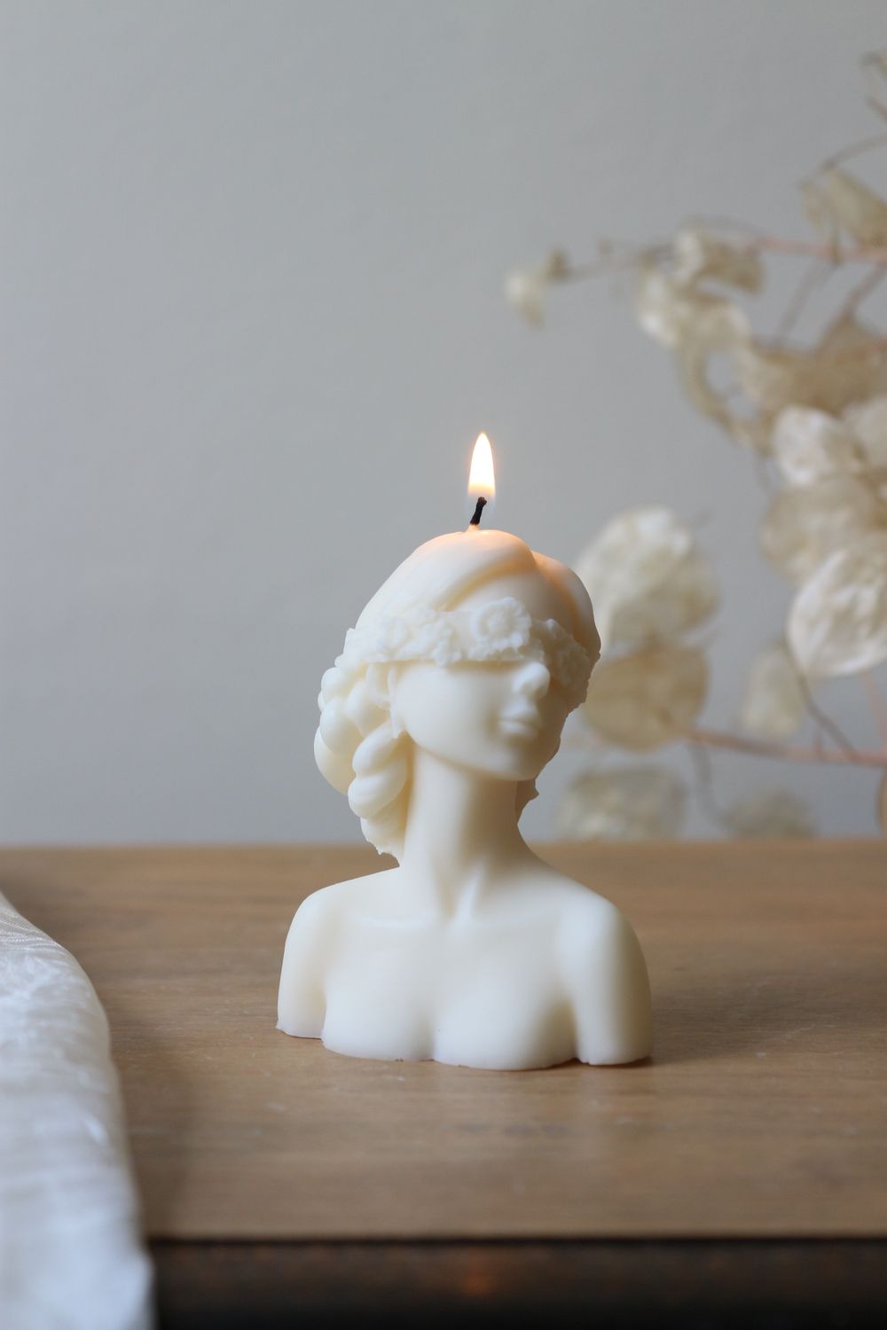 Candela decorativa in cera naturale bianca che rappresenta la dea bendata, accesa