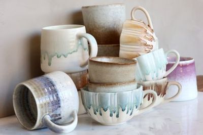 Assorted ceramic mugs and cups stacked together, with softly glazed finishes in earthy and seafoam tones.