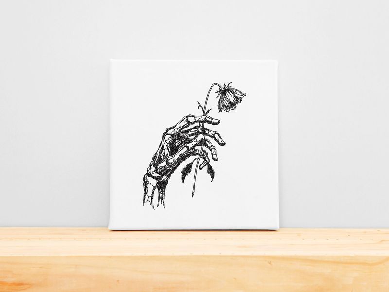 Black machine embroidery of a skeletal hand holding a wilted flower on a white stretched canvas frame. Dark academia wall art