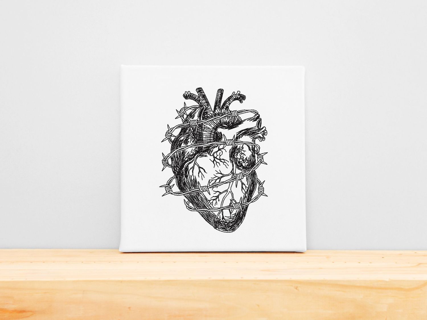 High-precision black embroidery of an anatomical heart wrapped in barbed wire, mounted on a white stretched canvas frame.