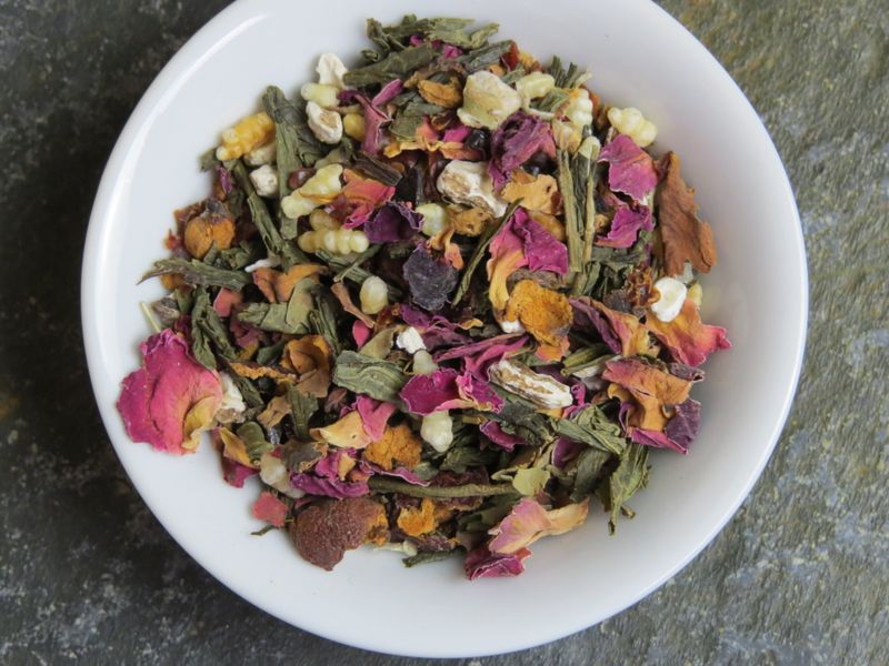 Looking down into a small white bowl filled with a blend of genmaicha, hawthorn berries, dandelion root, and bits of rose.