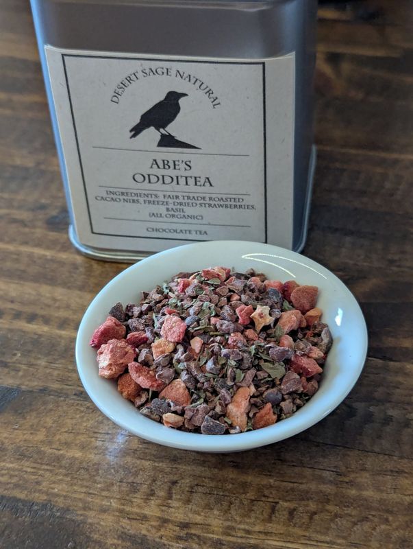 A small white bowl full of a blend of cacao nibs, strawberries, and basil sits in front of a tin labeled "Abe's OddiTea"