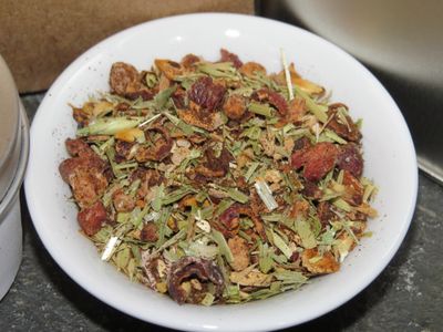 A small white bowl full of a blend of hawthorn berries, bits of green herbs, barley, ginger, with vanilla sprinkled over it.