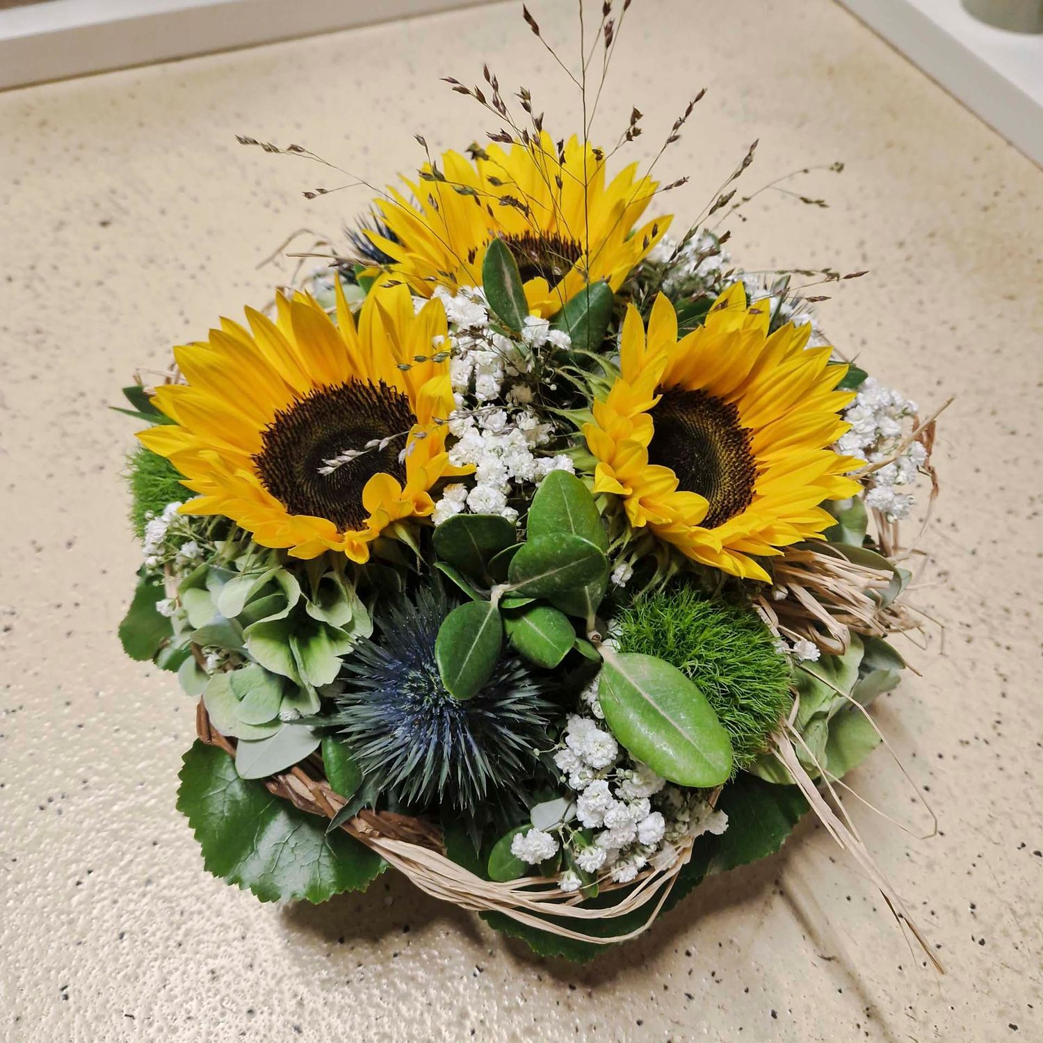 Gesteck mit drei Sonnenblumen, Schleierkraut und Grün, in Korb Gesteck mit drei Sonnenblumen, Schleierkraut und Grün, in Korb