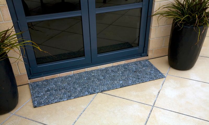Handmade stonemat with natural grey stones in a random pattern, placed at a backdoor leading to a patio