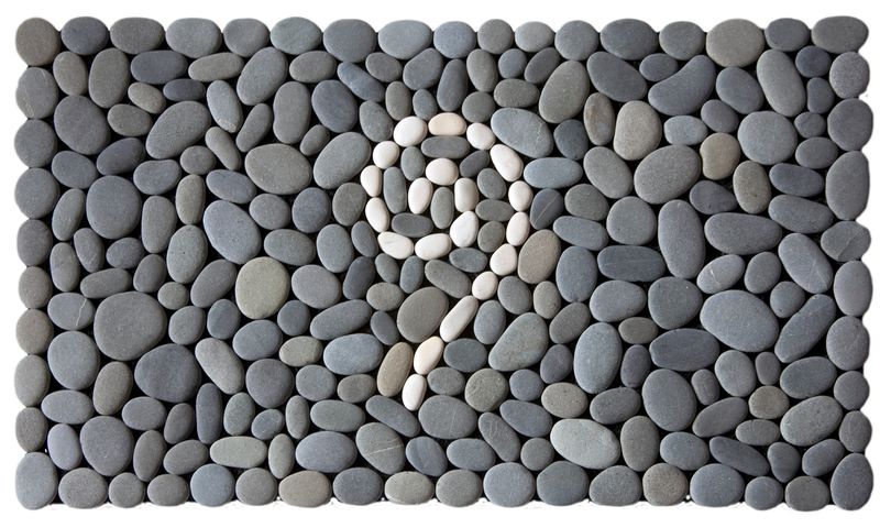 Koru of the Sky Stonemat featuring a vertical white koru spiral reaching upward, surrounded by natural grey stones