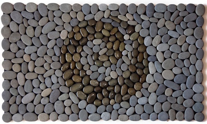 KORU OF THE SEA Stonemat featuring a polished koru spiral surrounded by natural grey stones in a dynamic handmade design.