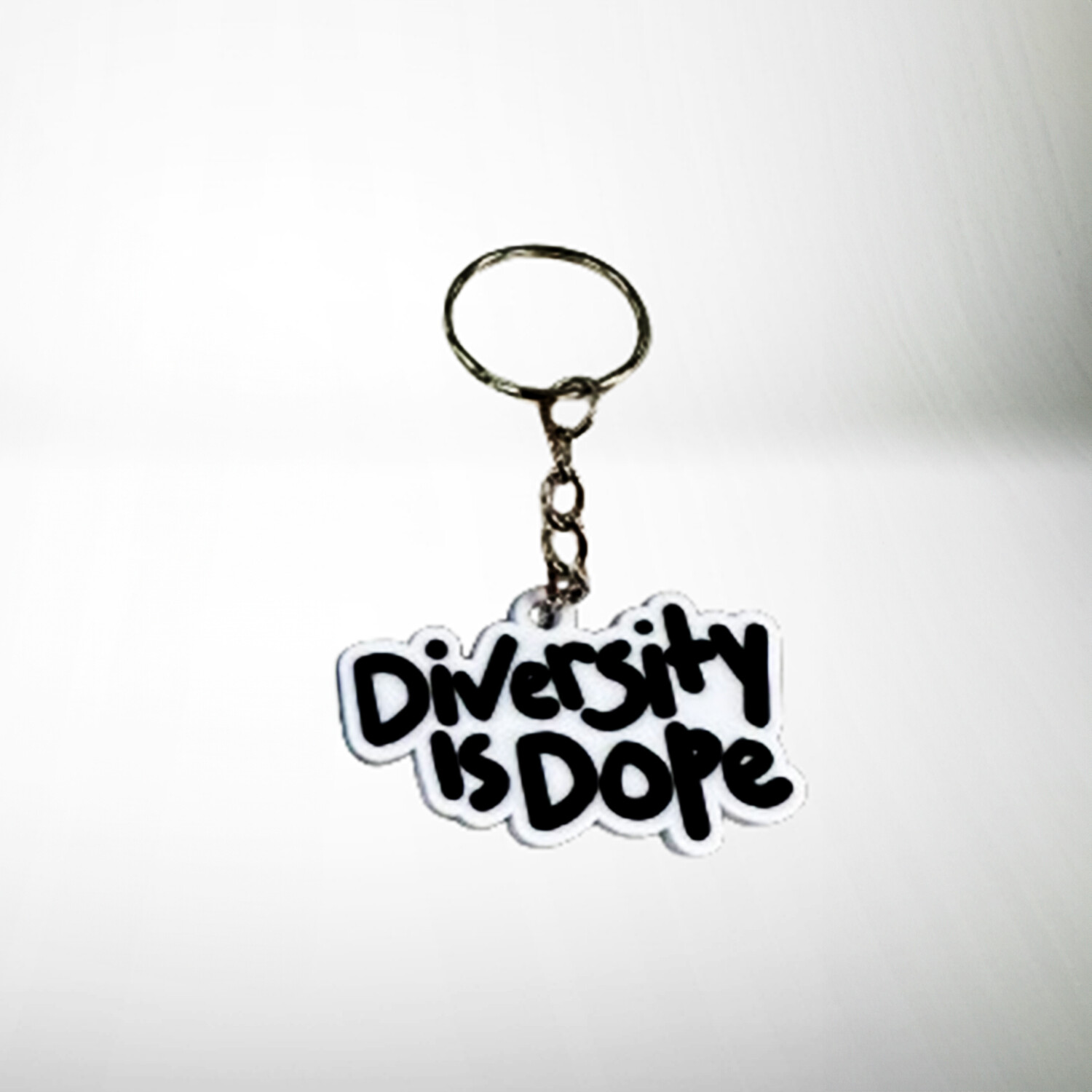 A keychain with a slogan that reads &quot;diversity is dope&quot; in stylized black and white lettering, placed on a plain white background.