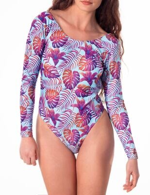 Sustainable tropical high-end long-sleeve one-piece swimsuit with open back, featuring bold purple and orange palm leaves and vibrant hibiscus blooms on a pastel light blue background worn by a woman.