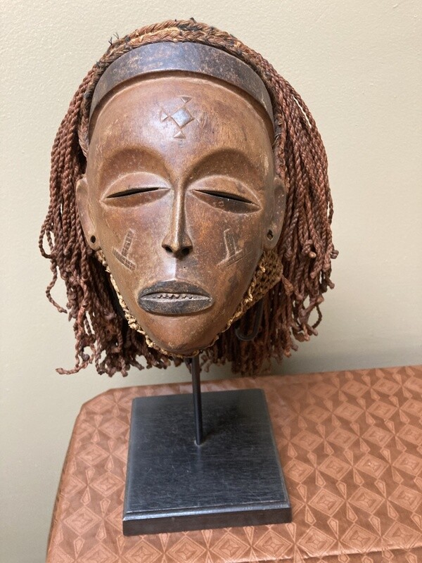 “Mwana Pwo” mask of the Chokwe (Tchokwe or Bajokwer) of Angola. Pwo is their word for woman. It represents a young woman who has been fully trained and is ready for marriage. Stand is included. Total