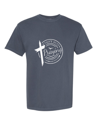 Denim colored t-shirt with Don't Stop Praying in a circular graphic with a large worn cross. Available in 2-4X, 100% Cotton