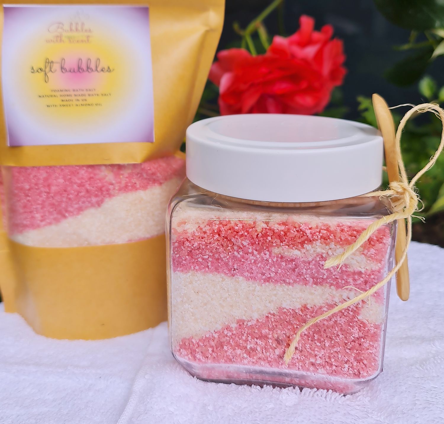 Soft Bubbles foaming bath salts by Bubbles with Scent, featuring pink and white layered salts in a clear glass jar, accompanied by a refill pouch, set against a floral background.