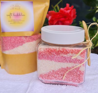Soft Bubbles foaming bath salts by Bubbles with Scent, featuring pink and white layered salts in a clear glass jar, accompanied by a refill pouch, set against a floral background.