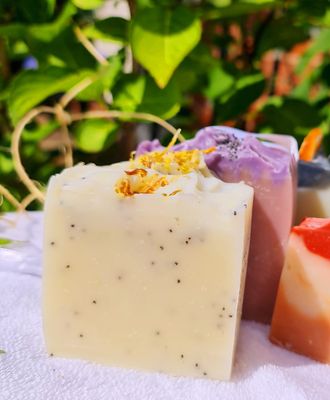 Handcrafted lemon and poppy seed exfoliating bar soap with a natural creamy yellow color, adorned with dried flower petals on top. This vegan, cruelty-free soap is displayed outdoors, highlighting its natural ingredients and gentle exfoliating properties, perfect for refreshing and nourishing your skin.