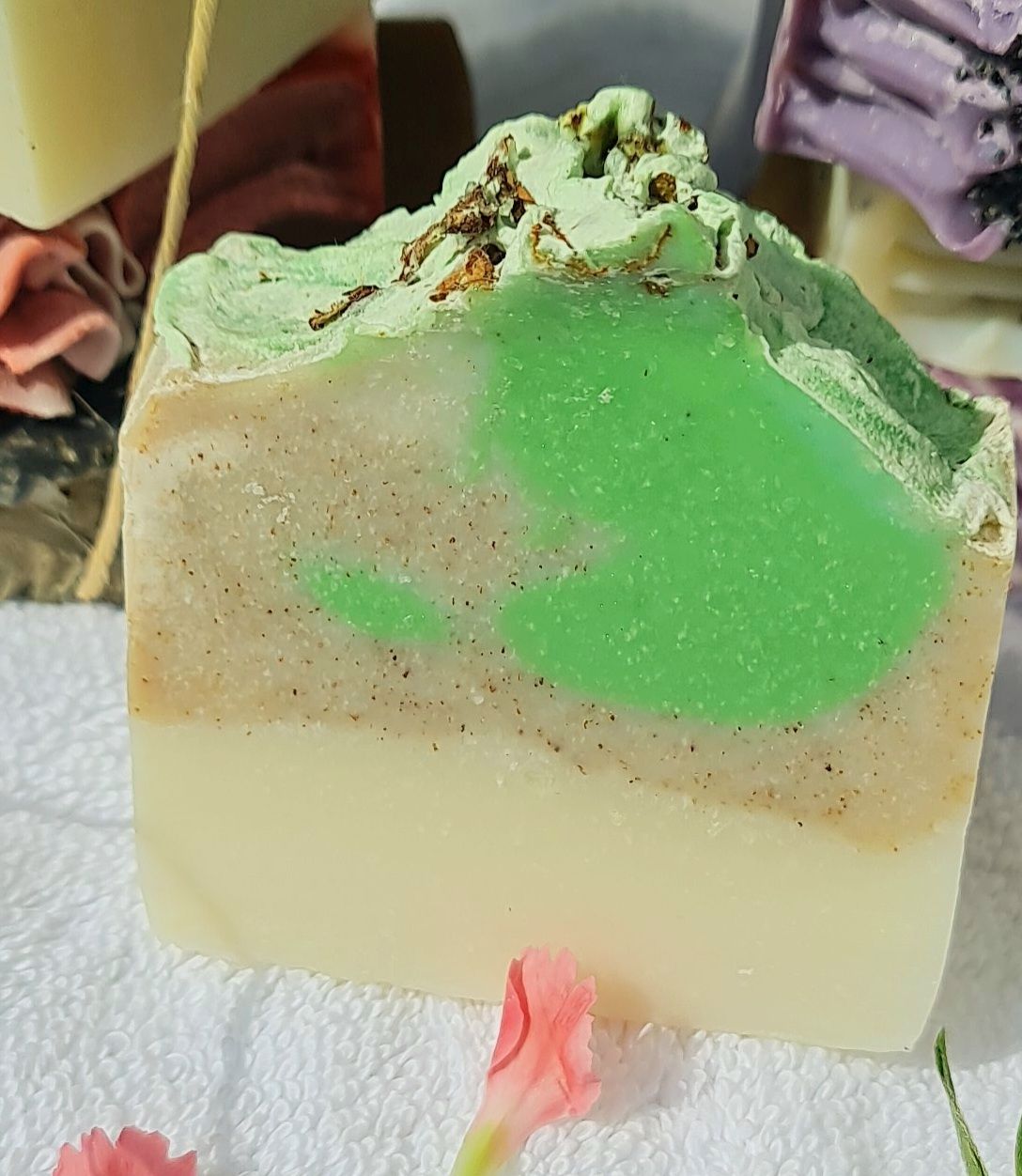 Mint Lemon handmade soap bar with a vibrant green swirl on top of a beige and white base, showcasing its natural and artisanal quality, placed on a white towel with delicate pink flowers in the foreground