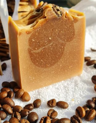 Handcrafted cold process soap bar with a rich coffee fragrance, featuring a swirl design in shades of brown, surrounded by roasted coffee beans, set on a white towel