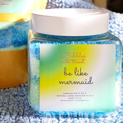 Jar of &#39;Be Like Mermaid&#39; foaming bath salts by Bubbles with Scent, featuring a colorful label and blue-green salts, set against a textured blue background.