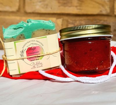 Handcrafted strawberry soap bar and jar of strawberry scrub placed on a red cloth background, showcasing plant-based exfoliating skincare products