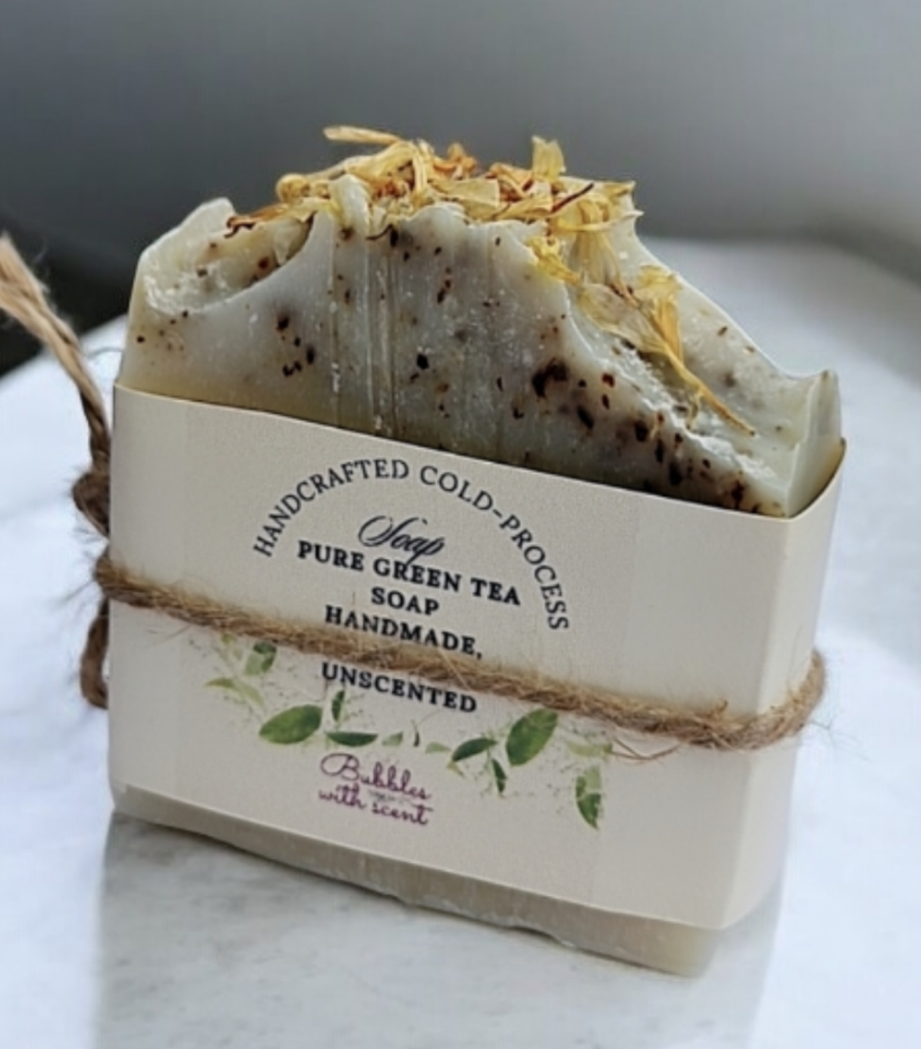 A handcrafted, cold-process soap bar labeled &quot;Pure Green Tea Soap&quot; from Bubbles with Scent. The soap is unscented, natural, and handmade, wrapped with a simple, eco-friendly paper and twine packaging, featuring dried botanicals on top