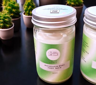 Bubbles with Scent Magnesium Body Foot Balm in a glass jar with a green gradient label, featuring the scent &#39;Mint with Honey.&#39; The jar is placed on a dark surface, surrounded by small potted cacti, highlighting the product&#39;s fresh and natural appeal