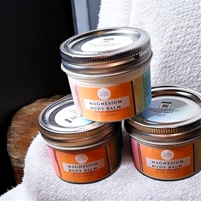 Stacked jars of Bubbles with Scent Magnesium Body Balm in Sweet Orange with Honey scent. Each jar has an orange gradient label, emphasizing the bright and uplifting citrus qualities of the product. The jars are arranged on a soft white fabric, giving a cozy and inviting feel