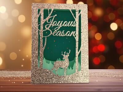 3D SVG template for a four-panel Christmas card designed for Cricut and other cutting machines. This simple card gives the illusion of a layered artwork. It features a deer among birch trees, tree-topped mountains set against a peaceful snowy background, and the words Joyous Season.