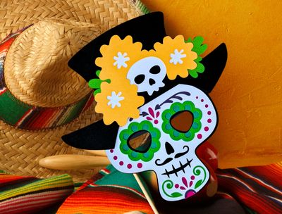 A colorful Dia de Los Muertos paper mask SVG template, depicting a Mexican gentleman with a hat, El Catrin, shown here displayed as decoration.  Perfect for a Cricut project, this paper mask can be used as a photo booth prop or decoration at Day of the Dead celebrations.