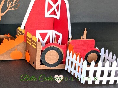 Detail view of the 3D SVG template for Cricut that makes a charming red barn accompanied by a tractor pulling a trailer filled with pumpkins,  Autumn trees and a classic white picket fence. The template includes a matching pumpkin-themed A7 envelope.