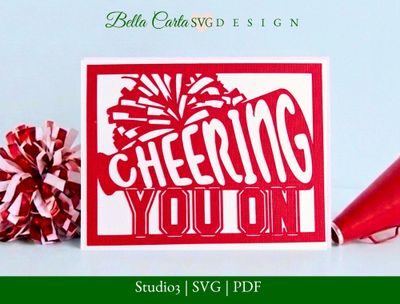 3D layered paper card featuring a cheerleader megaphone, pom-poms, and the words 'Cheering You On.' Designed as a layered SVG