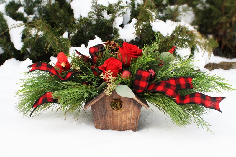 birdhouse winter flower arrangement with red roses and buffalo plaid ribbon, robbin, red berries, pinecones