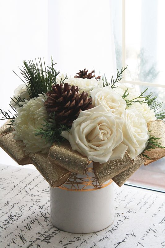 White rose flower arrangement with gold ribbon and pine in ceramic pot