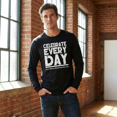 Male model wearing the black "CELEBRATE EVERY DAY" long-sleeve tee with white text branding in a sunlit brick loft setting.