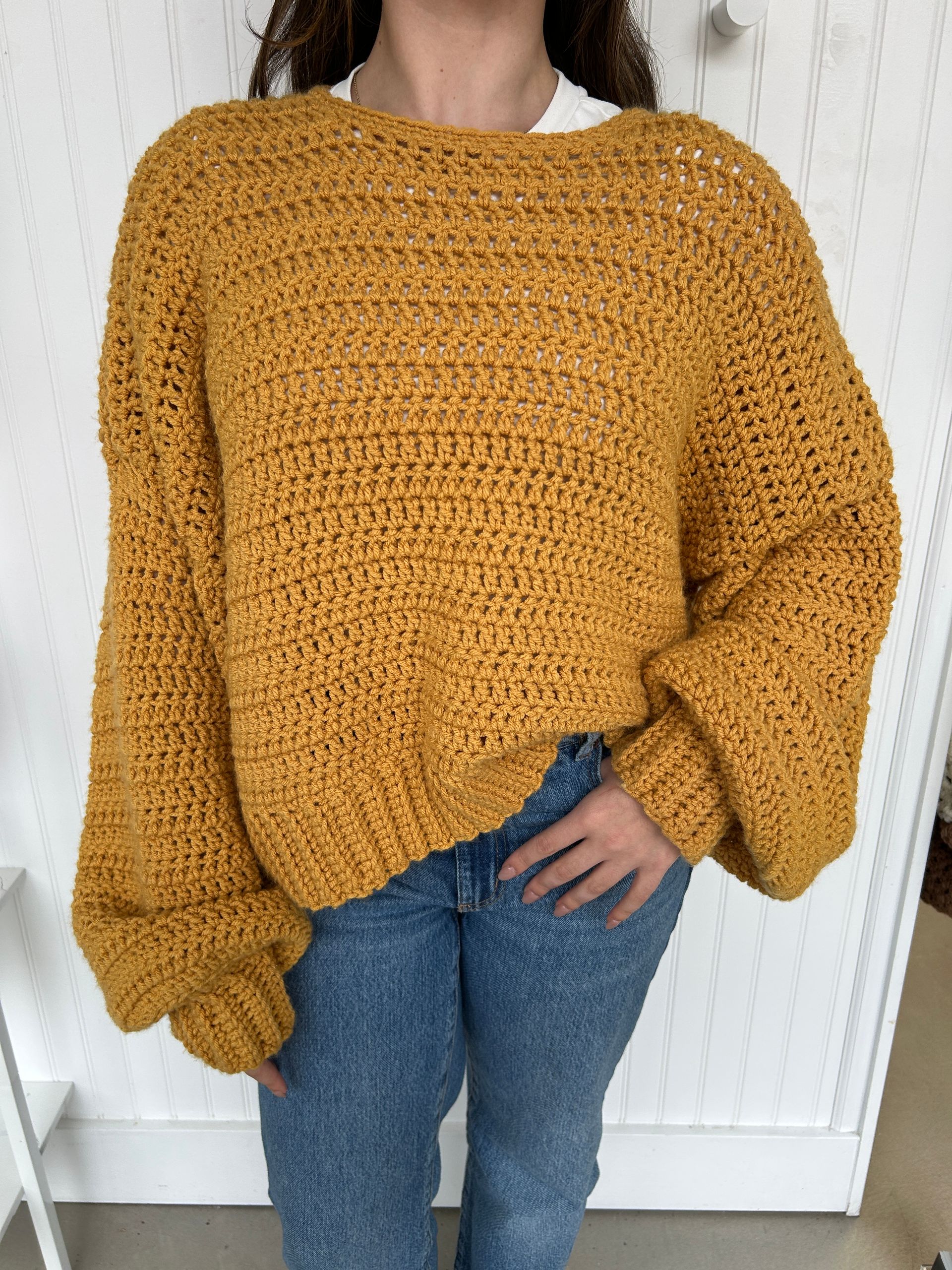 Mustard yellow handmade crochet sweater styled in a cozy indoor setting, perfect for fall and winter outfits.