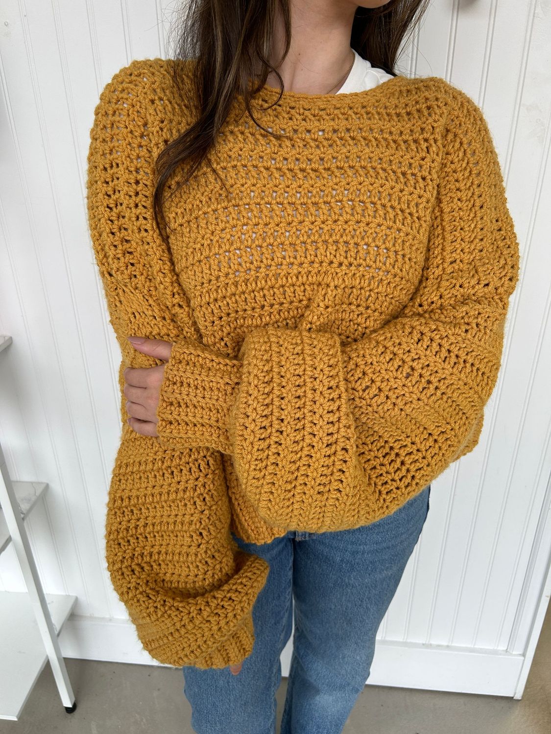 Mustard yellow handmade crochet sweater styled in a cozy indoor setting, perfect for fall and winter outfits.