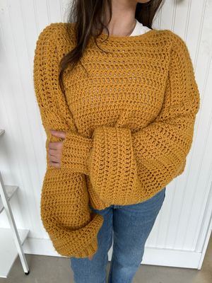 Mustard yellow handmade crochet sweater styled in a cozy indoor setting, perfect for fall and winter outfits.