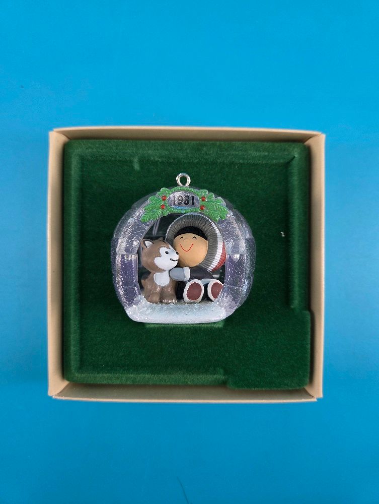 The ornament depicts a friendly winter scene and is displayed against a deep green felt.