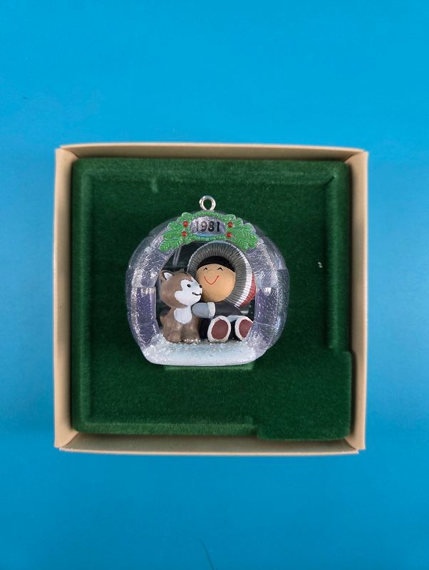 The ornament depicts a friendly winter scene and is displayed against a deep green felt.