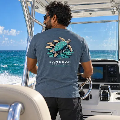 Man driving a boat wearing the Cayrunner Turtle Drift Unisex T-Shirt in heather slate, showing back sea turtle design
