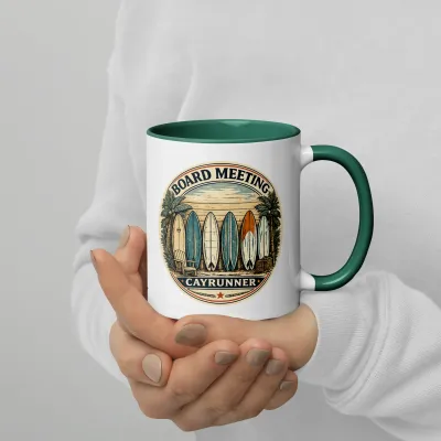Hands holding Cayrunner Board Meeting Coffee Mug with dark green handle, showing surfboard beach graphic design.