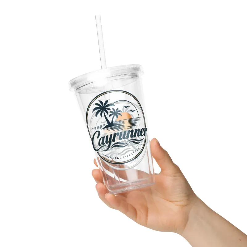 Hand holding Cayrunner Sunset Run Clear Plastic Tumbler with straw, showing palm tree coastal lifestyle logo.