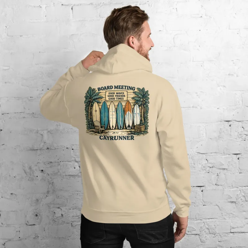 Man against a brick wall wearing the Cayrunner Board Meeting Unisex Hoodie, sand color, showing back surfboard design