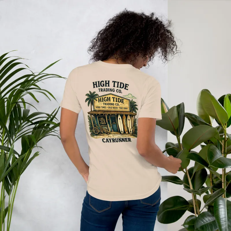 Woman among plants wearing the Cayrunner High Tide Trading Co. Unisex T-Shirt in cream, showing back beach shop design