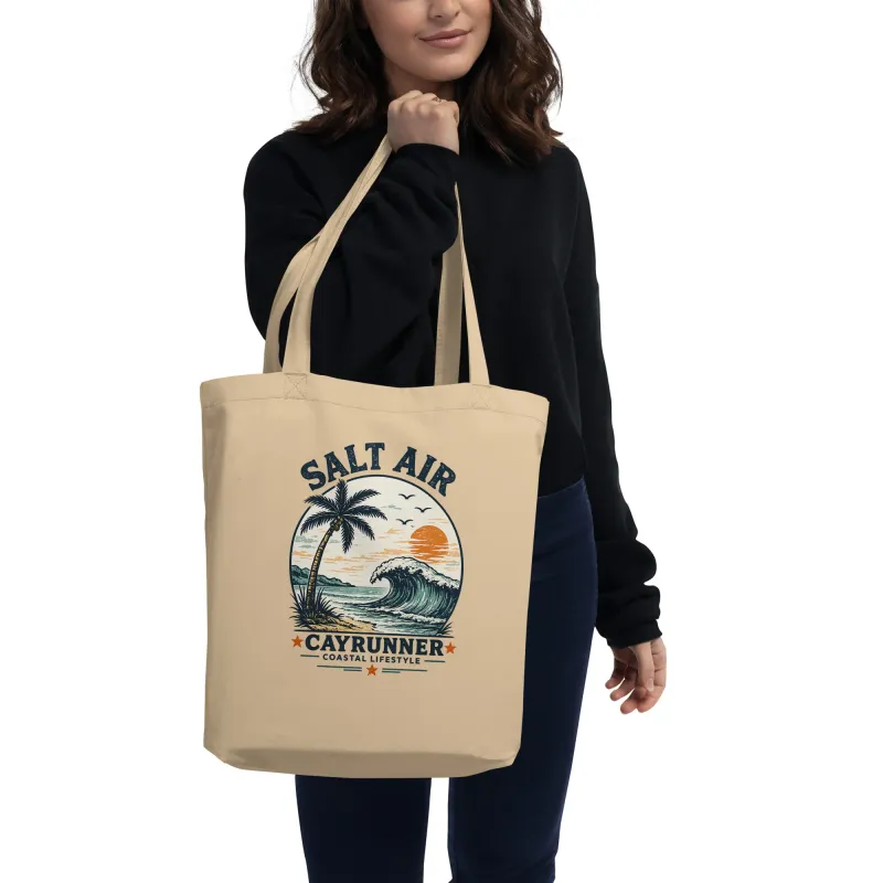 Woman carrying the Cayrunner Salt Air organic cotton tote bag with wave, palm tree, and sunset design