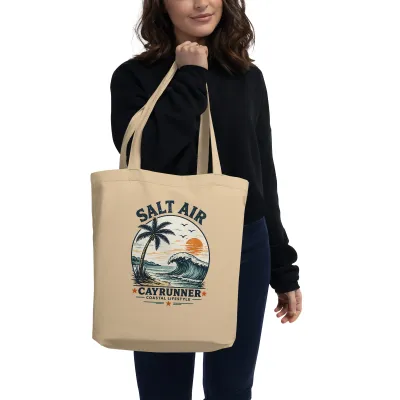 Woman carrying the Cayrunner Salt Air organic cotton tote bag with wave, palm tree, and sunset design