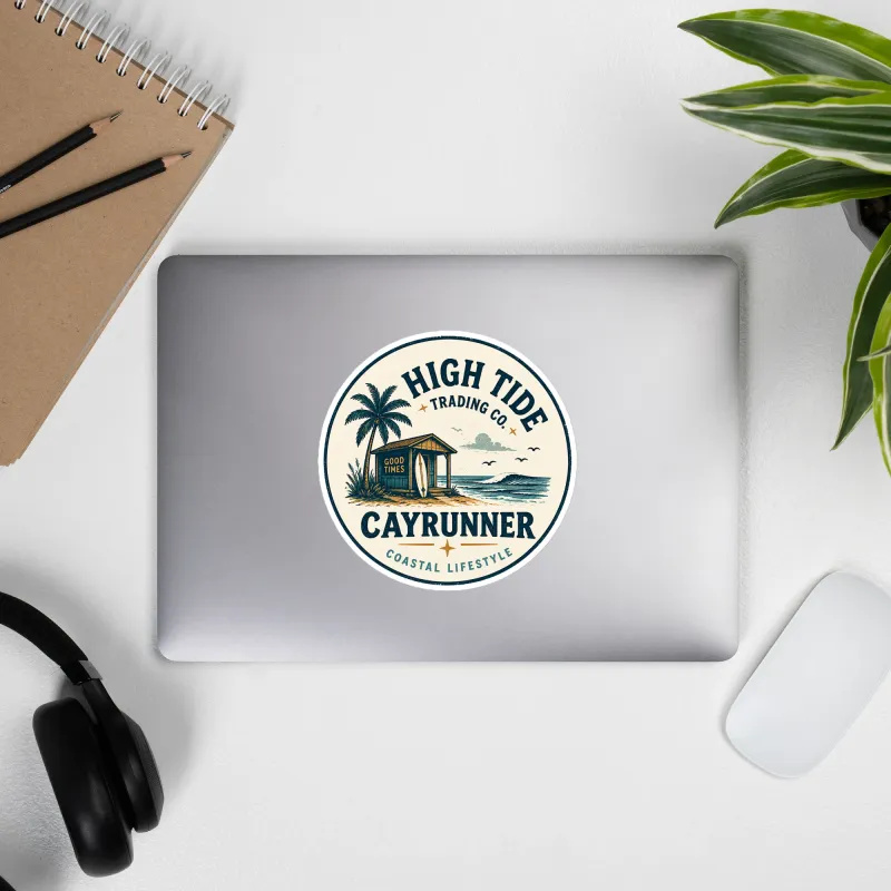 Cayrunner High Tide Trading Co. sticker on a laptop lid, beach hut and palm tree design, desk with plants nearby.