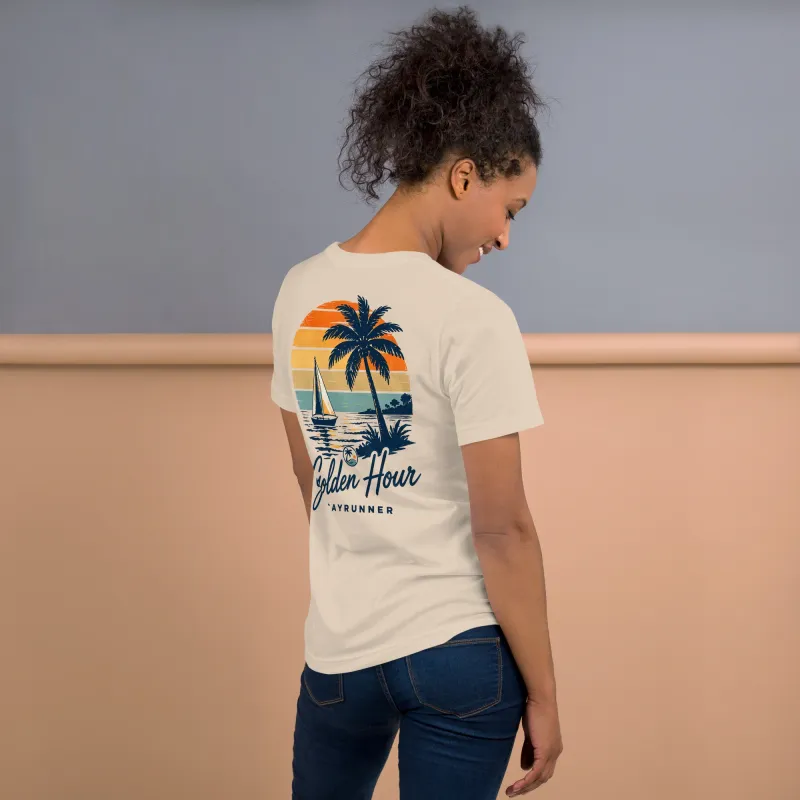 Woman wearing Cayrunner Sunset Sail unisex t-shirt in soft cream, side back view showing "Golden Hour" sailboat design.